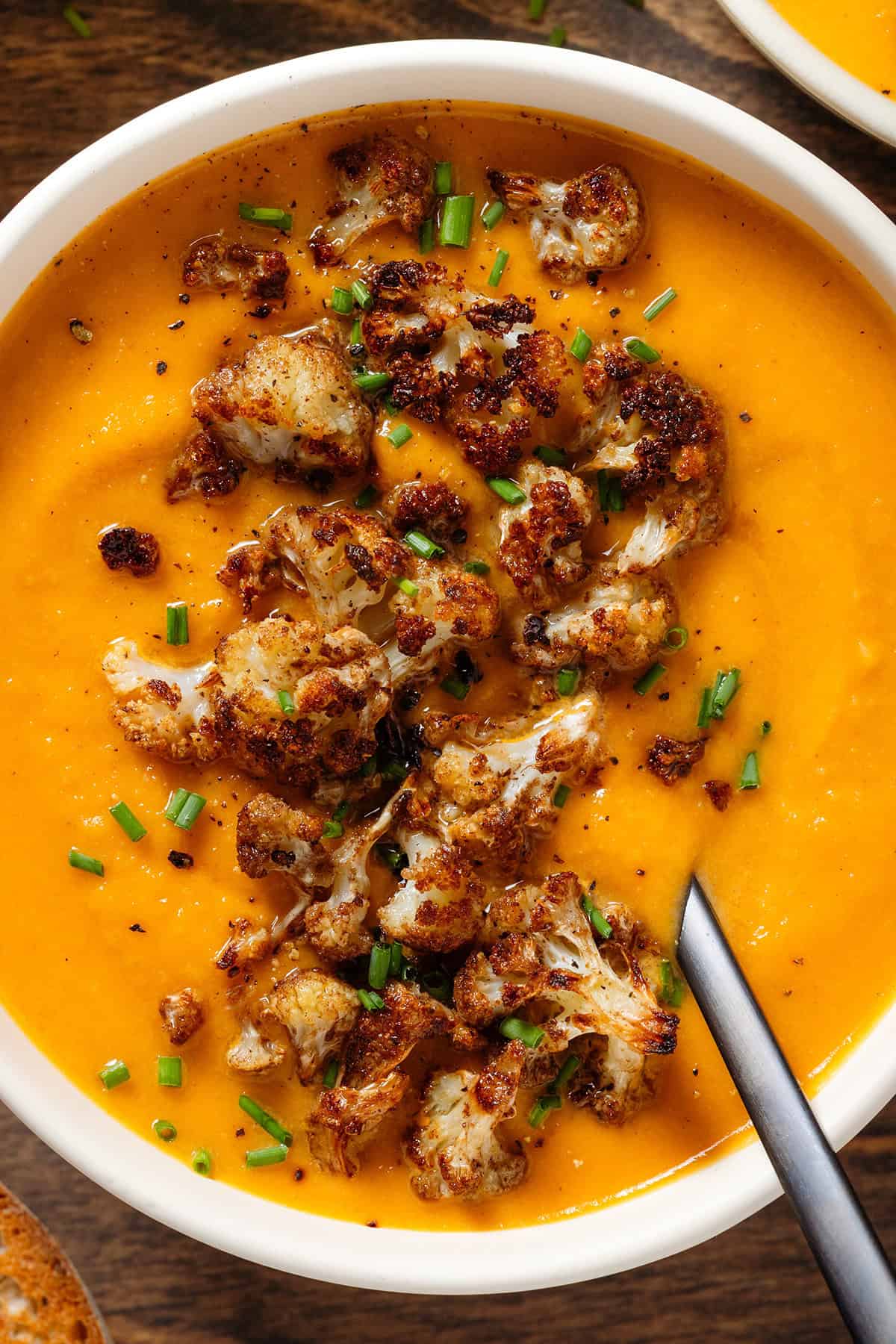 A white bowl with creamy sweet potato soup with caramelized cauliflower florets and chopped chives on top.