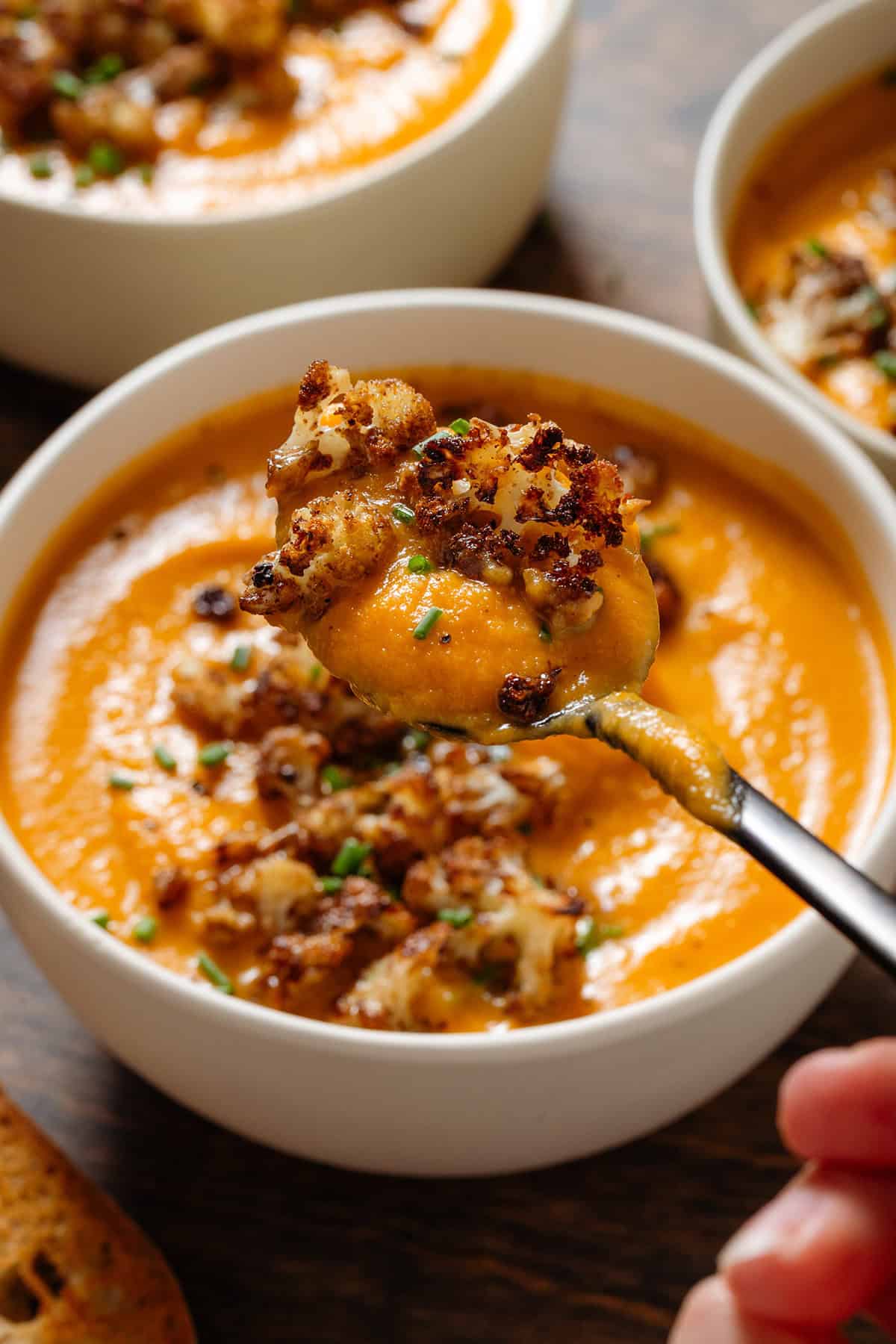 A white bowl with thick and creamy sweet potato soup with roasted cauliflower on top and a spoon scooping up some of both to show the caramelized texture.