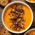 A white bowl with creamy sweet potato soup with caramelized cauliflower florets and chopped chives on top.