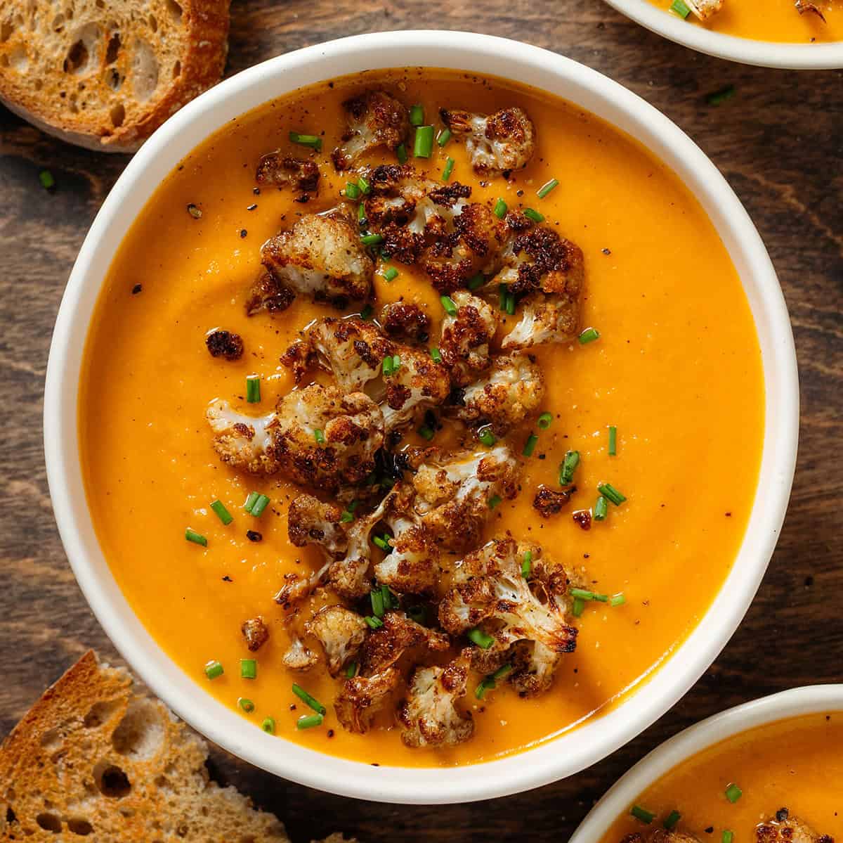 A white bowl with creamy sweet potato soup with caramelized cauliflower florets and chopped chives on top.