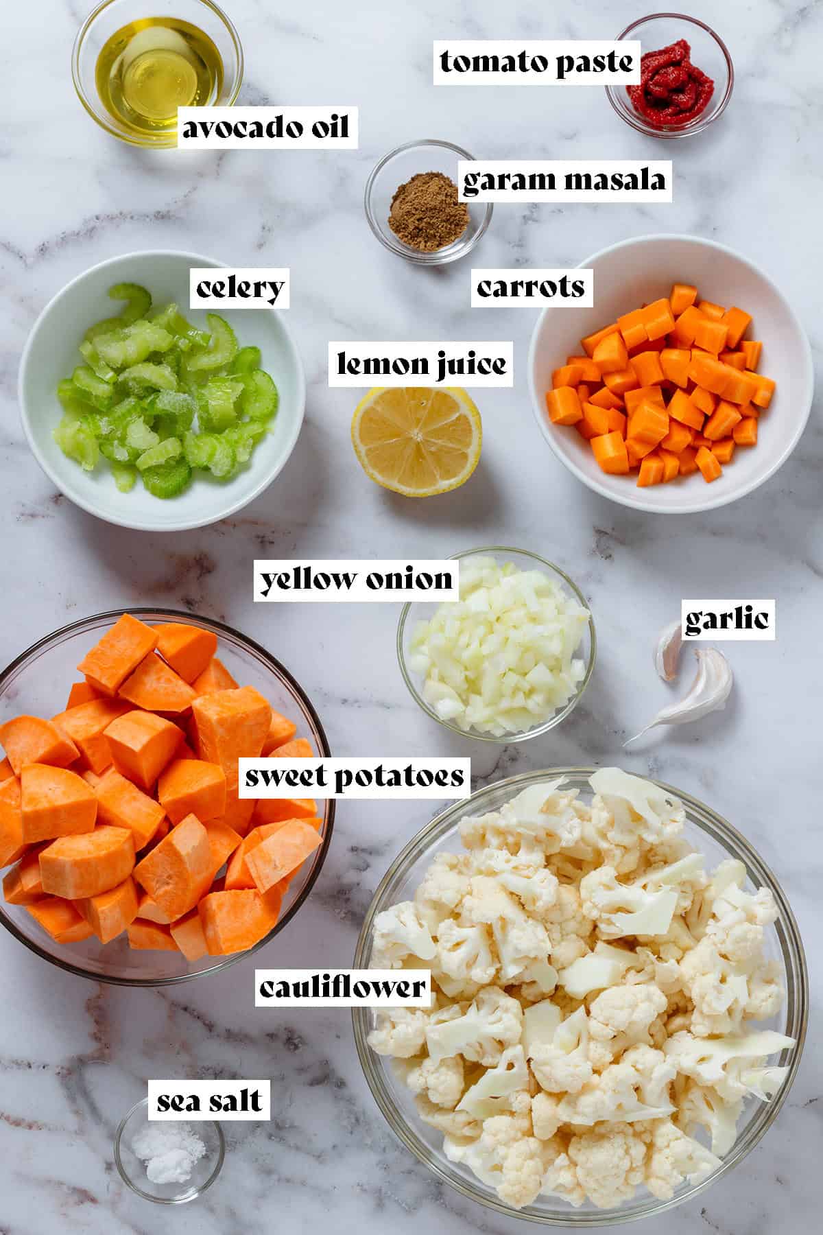 Small and large bowls with diced sweet potatoes, cauliflower florets, diced carrots, celery, onion, and spices.