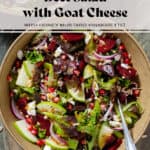 Salad with steamed beets, sliced apple, goat cheese, pomegranate arils, goat cheese, and whole grain mustard vinaigrette in a brown bowl with a fork inserted on the right.