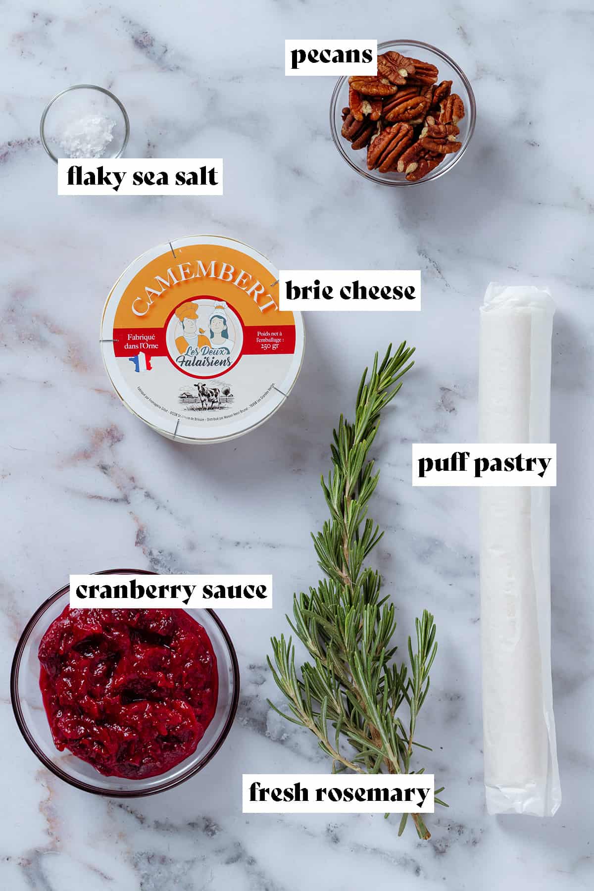 Rolled puff pastry, brie cheese, fresh rosemary sprig, pecans, sea salt, and cranberry sauce in small glass bowls with text overlay.
