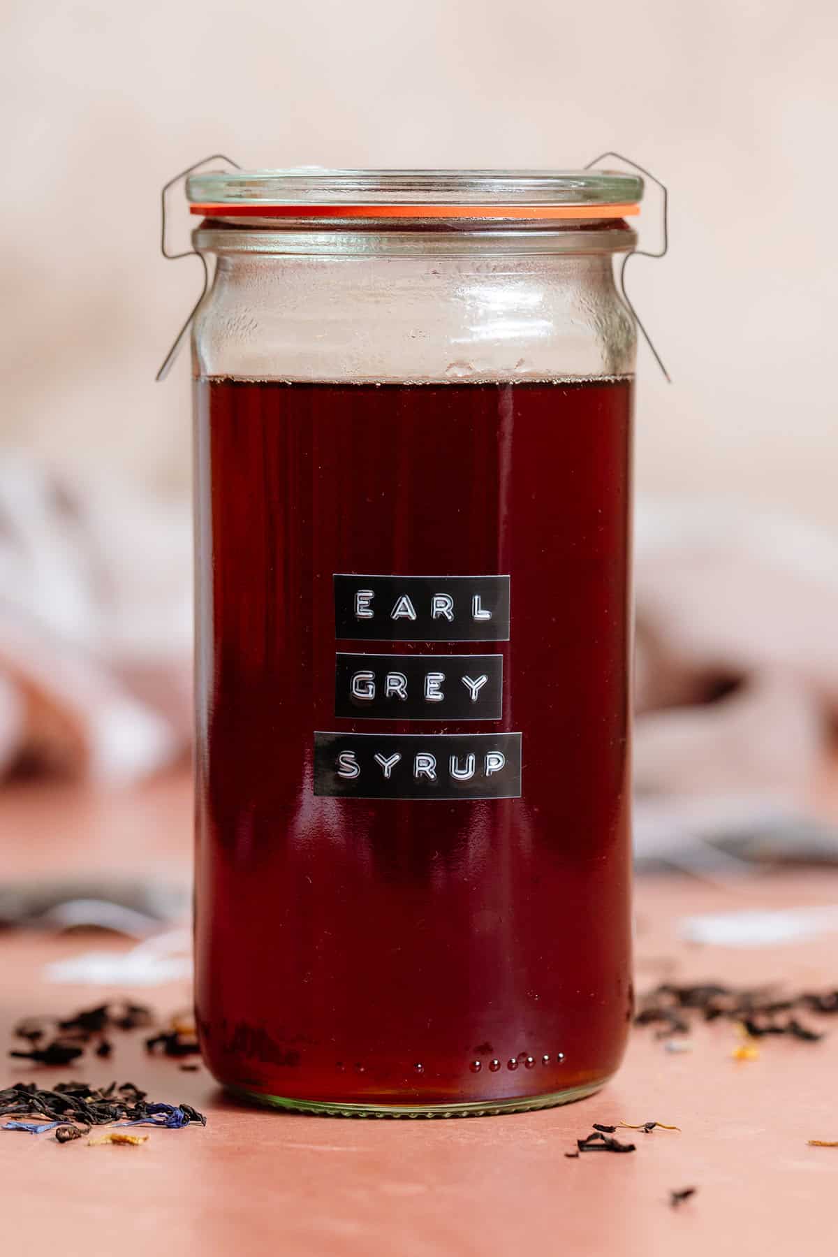 A tall glass jar with earl grey syrup closed with a lid with a black embossed label on the front of the jar.