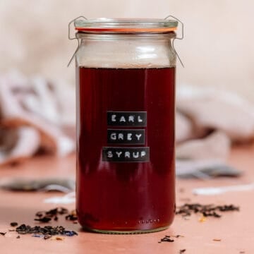 A tall glass jar with earl grey syrup closed with a lid with a black embossed label on the front of the jar.