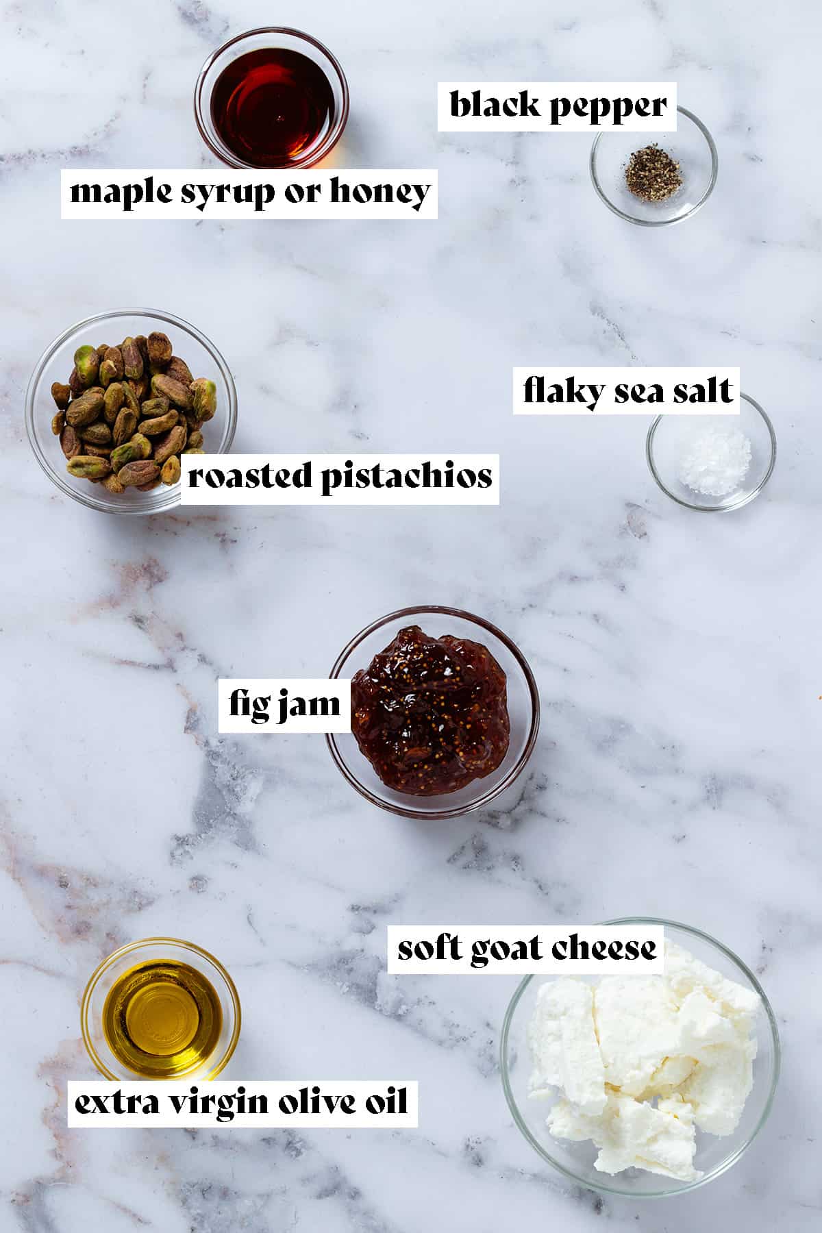 Ingredients in small glass bowls like soft goat cheese, fig jam, roasted pistachios, olive oil, and spices with text overlay.