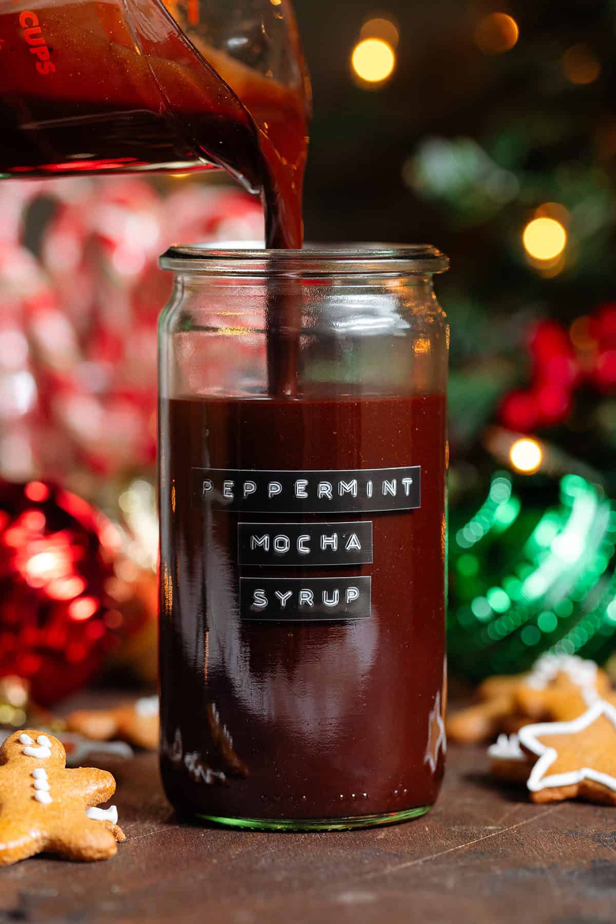 Rich chocolate peppermint syrup being poured into a tall glass jar with a black embossed label on the front.