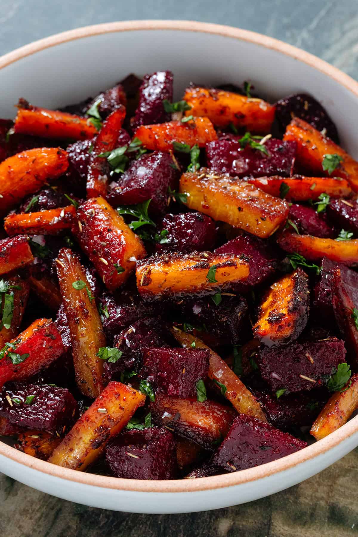 Caramelized roasted beets and carrots with balsamic vinaigrette garnished with chopped fresh parsley and flaky sea salt in a white bowl.
