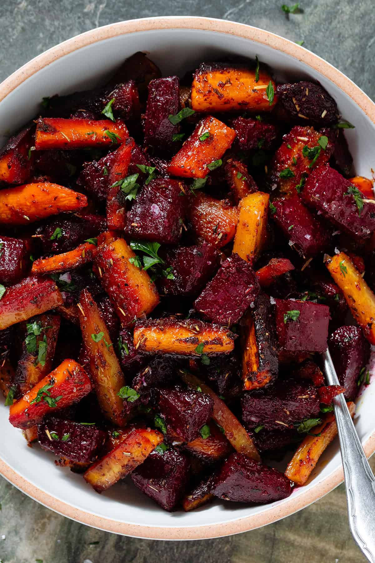 Caramelized roasted beets and carrots with balsamic vinaigrette garnished with chopped fresh parsley and flaky sea salt in a white bowl.