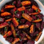 Caramelized roasted beets and carrots with balsamic vinaigrette garnished with chopped fresh parsley and flaky sea salt in a white bowl.