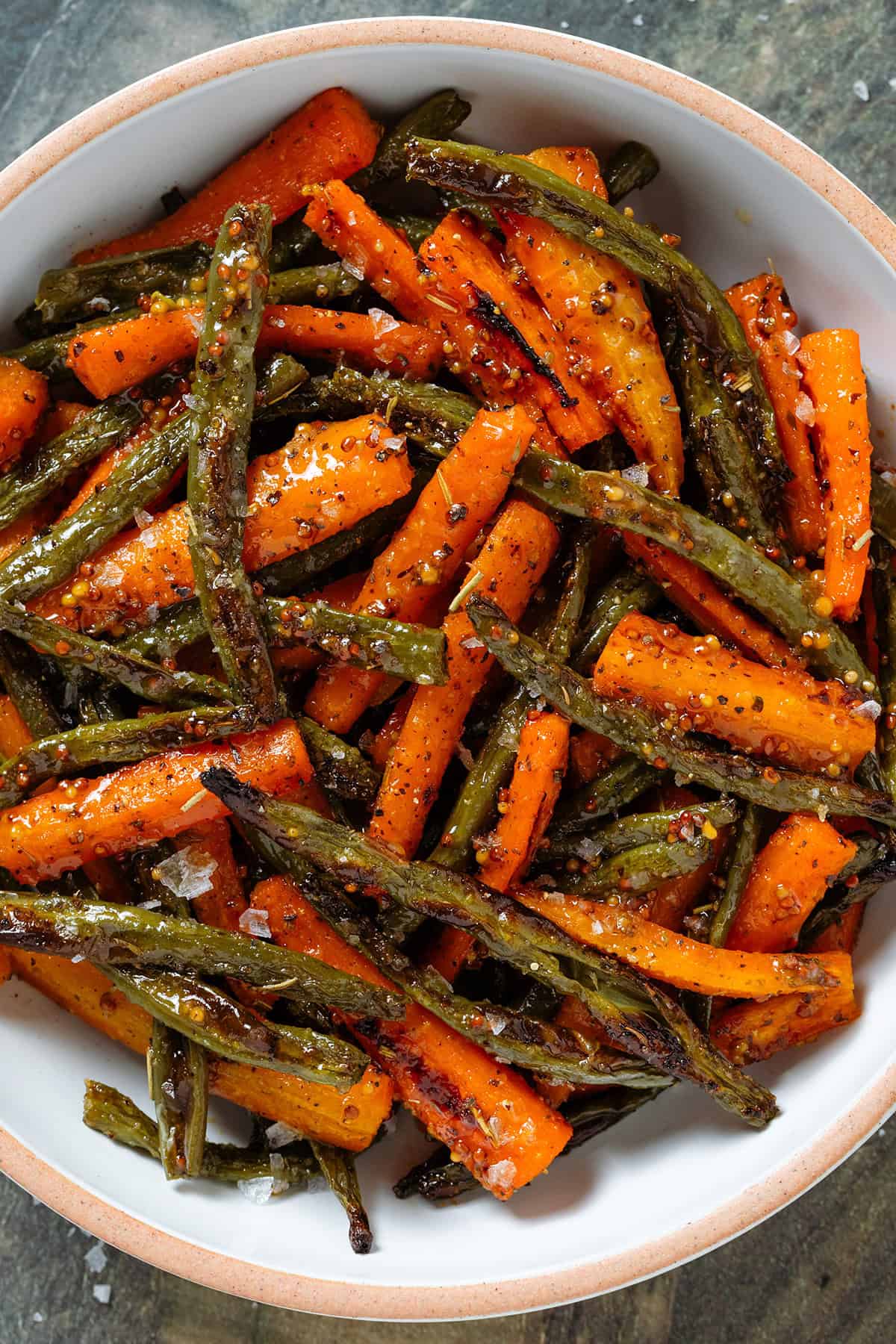 Roasted carrots and green beans with whole mustard vinaigrette and flaky sea salt in a white bowl with a beige rim.