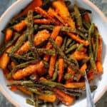 Roasted carrots and green beans with whole mustard vinaigrette in a white bowl with a beige rim with a fork inserted on the right.