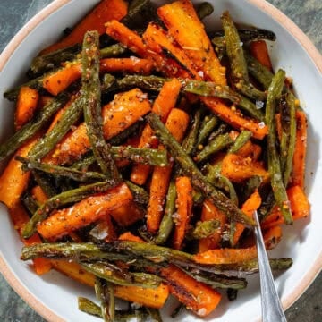 Roasted carrots and green beans with whole mustard vinaigrette in a white bowl with a beige rim with a fork inserted on the right.