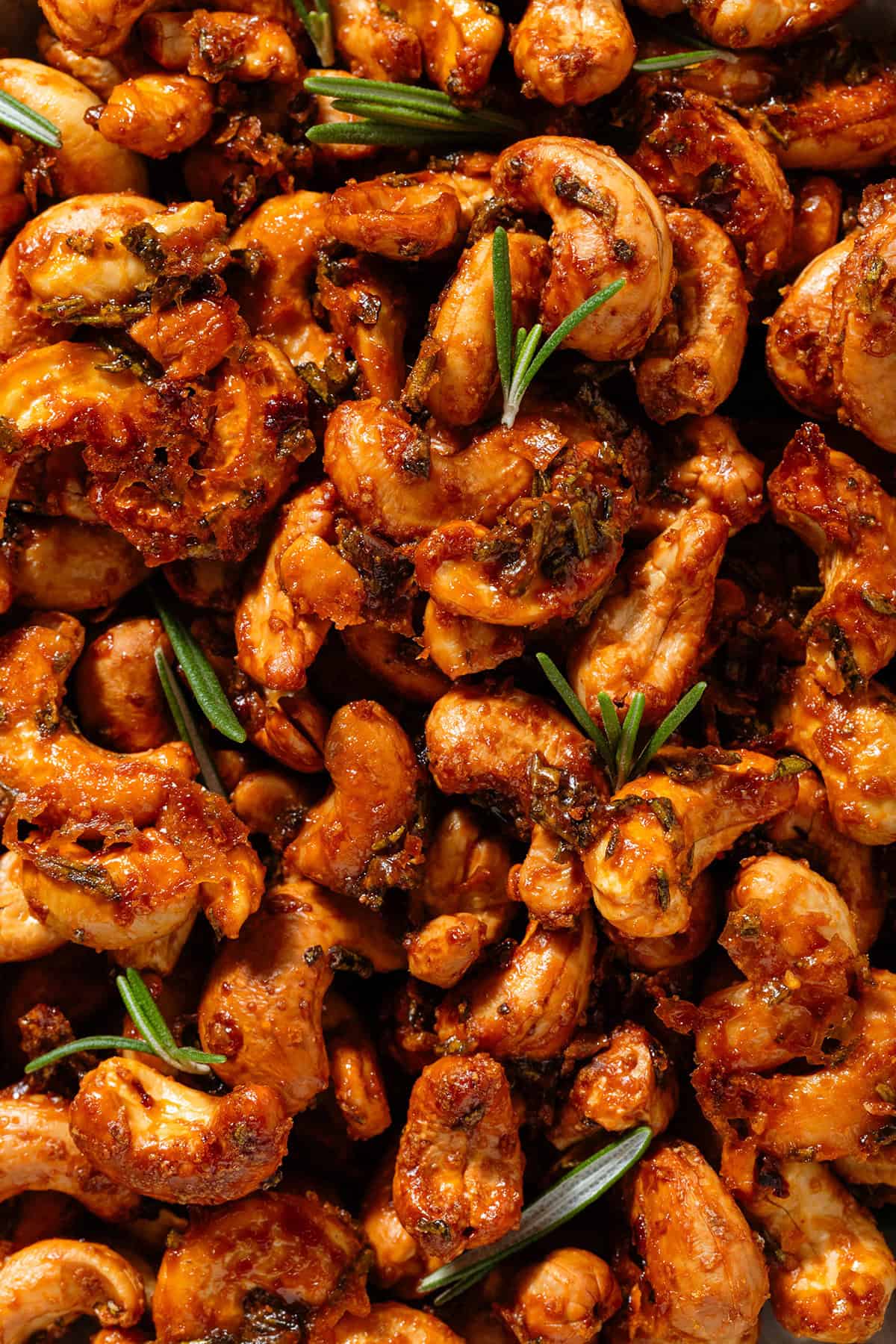 Golden caramelized roasted cashews garnished with fresh rosemary leaves.