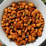 Golden roasted cashews with rosemary in a white ceramic bowl garnished with fresh rosemary.