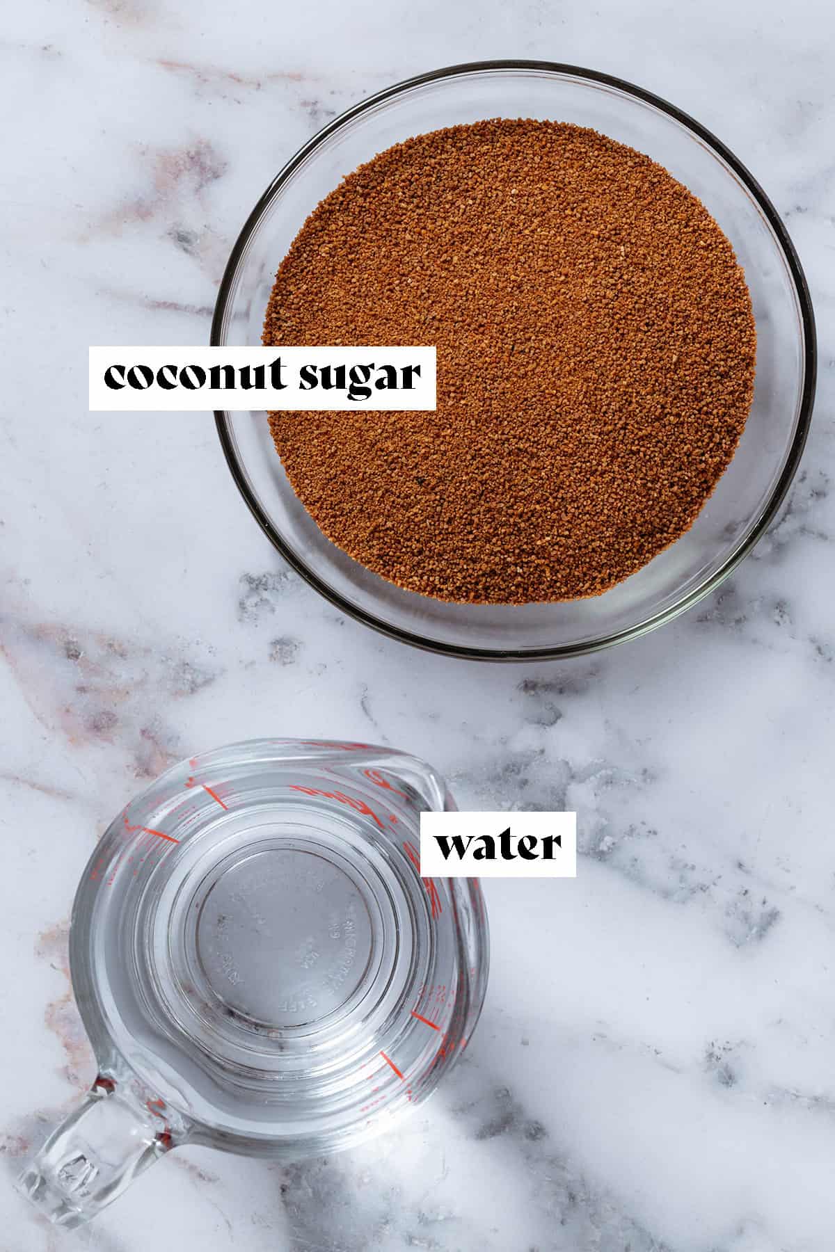 Coconut sugar in a glass bowl and water in a glass measuring cup on a marble background.