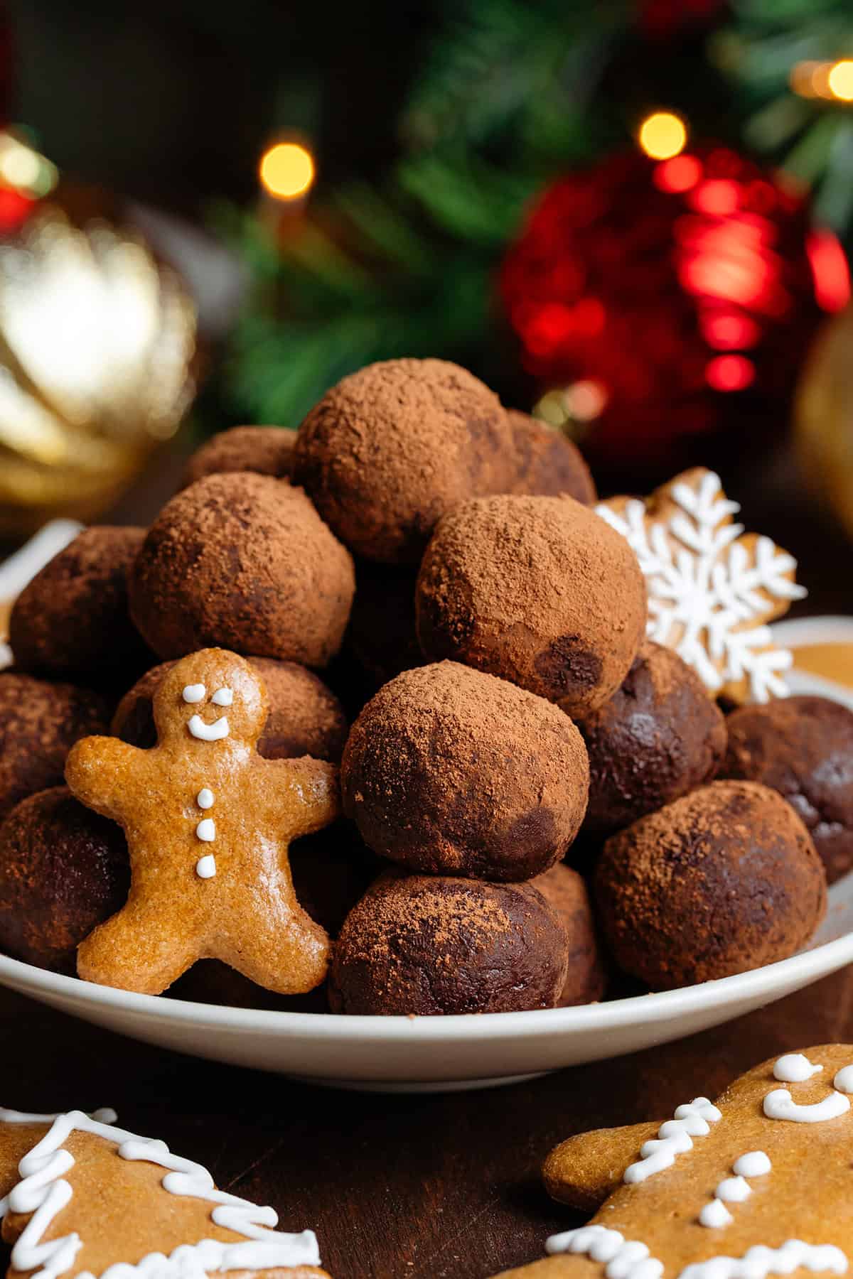 Energy balls rolled in cocoa powder stacked on a small beige plate garnished with mini gingerbread cookies.