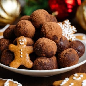 Energy balls rolled in cocoa powder stacked on a small beige plate garnished with mini gingerbread cookies.