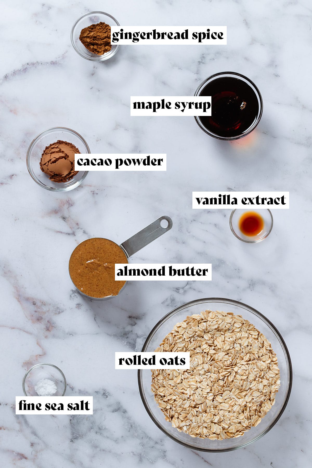 Ingredients like rolled oats, almond butter, maple syrup, cacao powder, and spices in small glass bowls with text overlay.