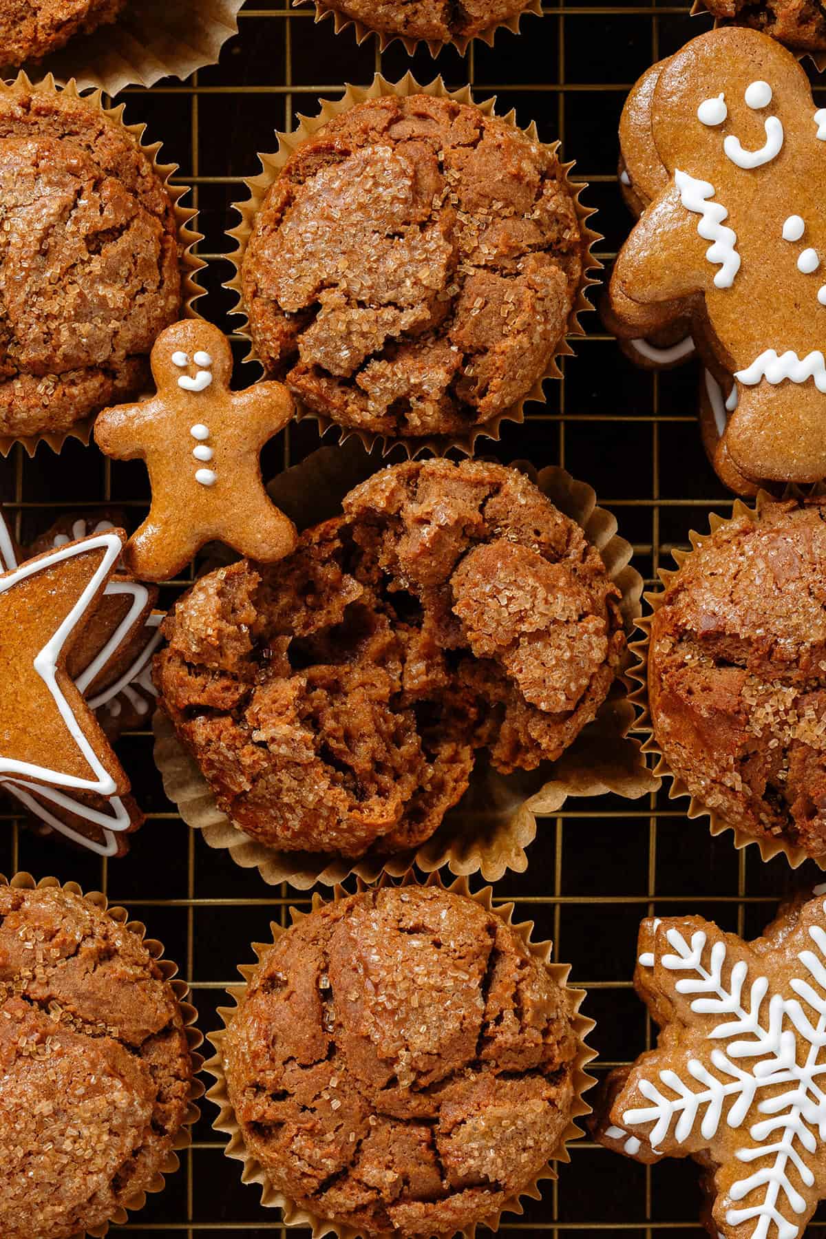 Gingerbread muffins on a gold cooling rack with gingerbread cookies in between them with the muffins in the middle broken in half to show the fluffy inside.