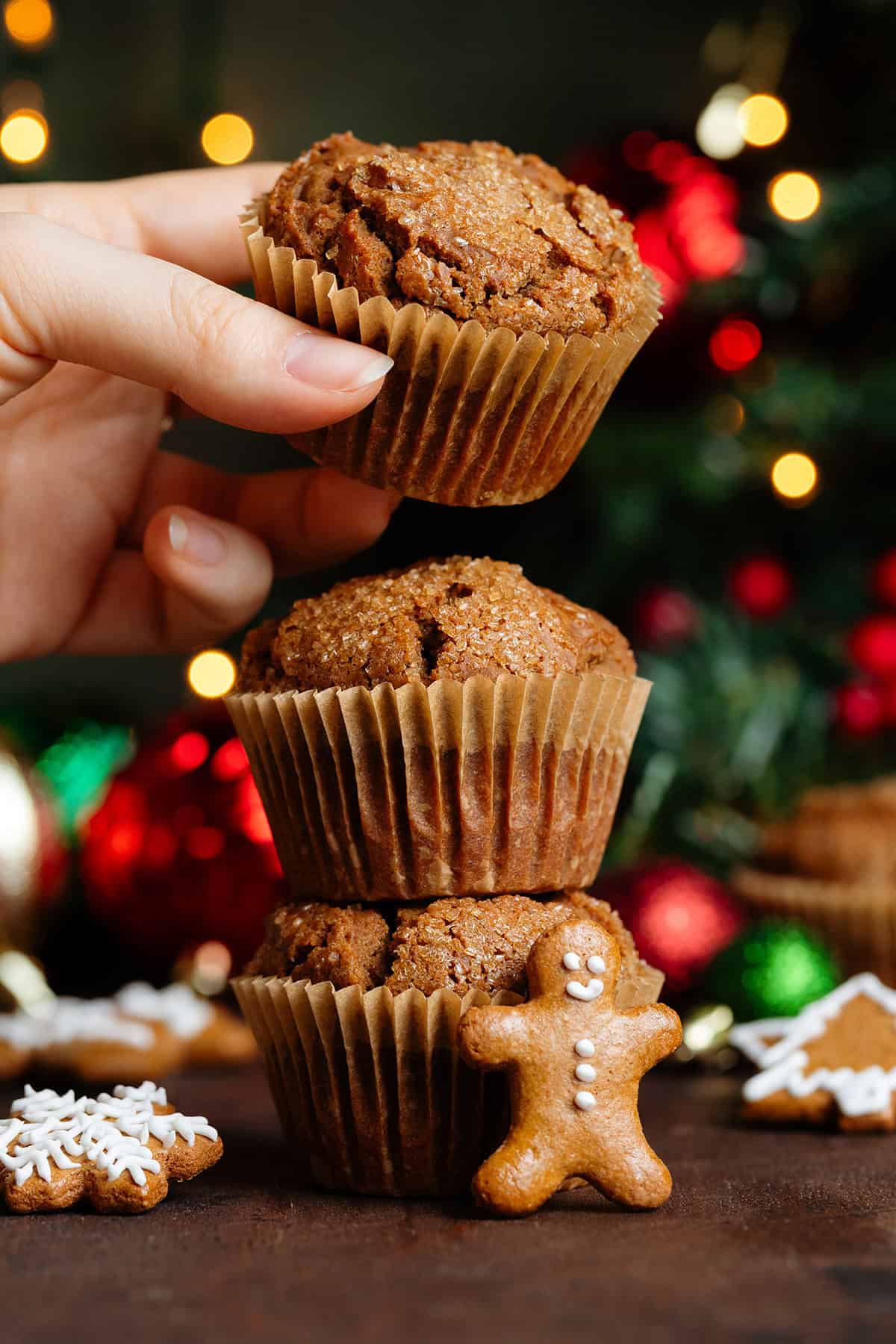 Three muffins stacked on top of each other and a hand grabbing the top one with a mini gingerbread man cooking leaning on the front of the muffins.