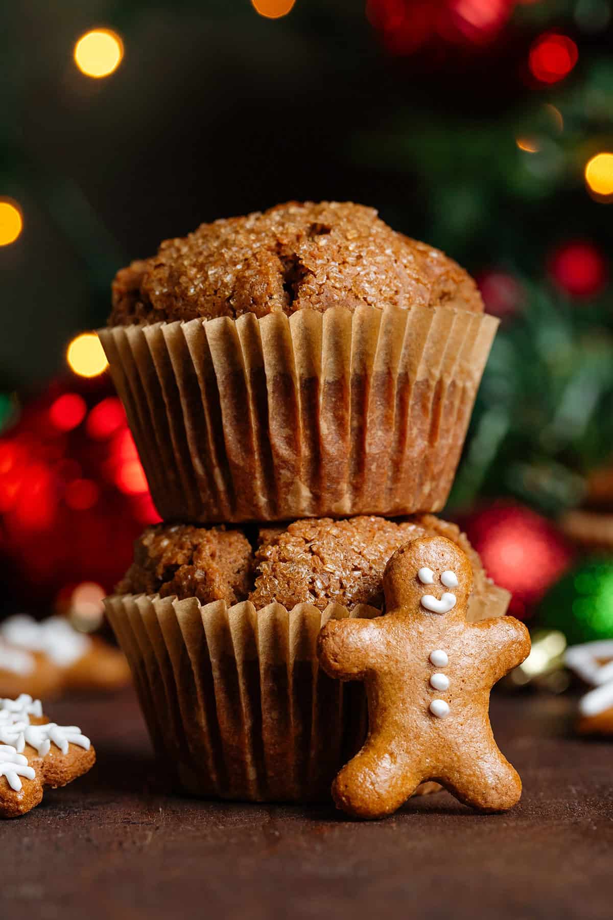 Two muffins stacked on top of each other with a mini gingerbread man leaning on the front of them and other gingerbread scattered cookies around.