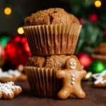 Two muffins stacked on top of each other with a mini gingerbread man leaning on the front of them and other gingerbread scattered cookies around.