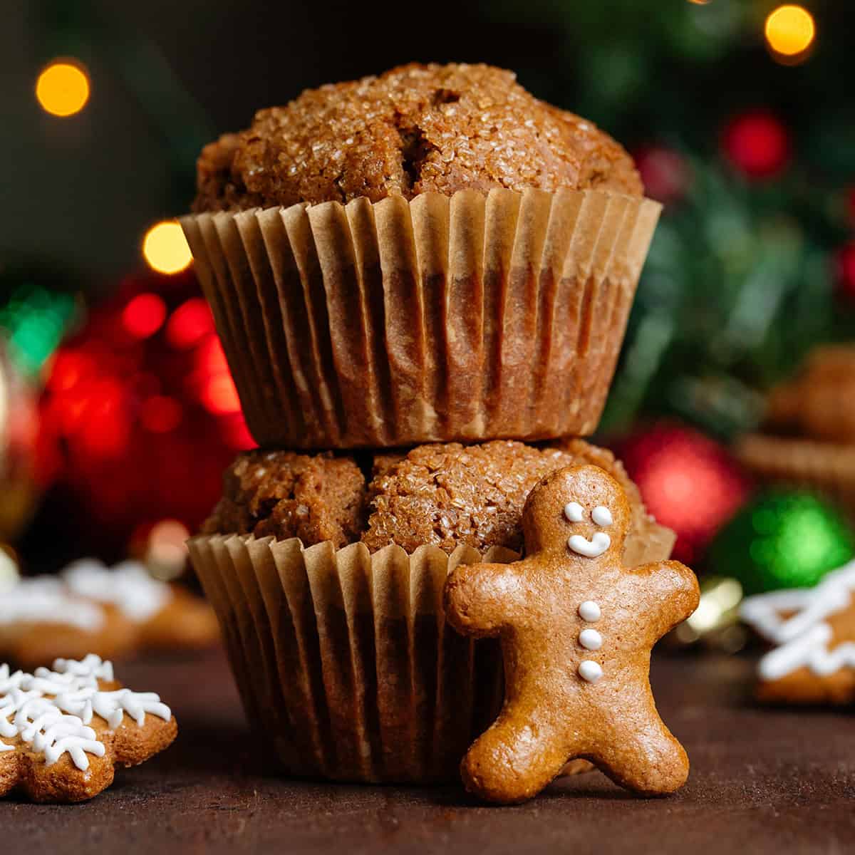 Two muffins stacked on top of each other with a mini gingerbread man leaning on the front of them and other gingerbread scattered cookies around.