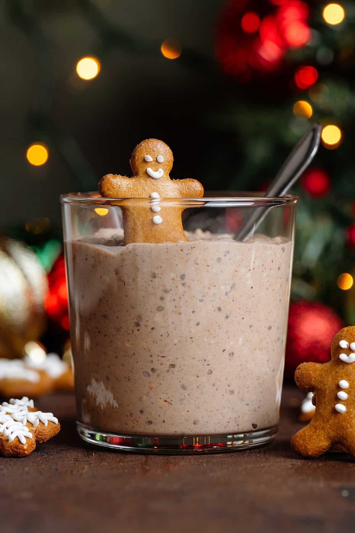 Overnight oats in a short glass topped with a small gingerbread man and a spoon in it with more gingerbread cookies around the glass.