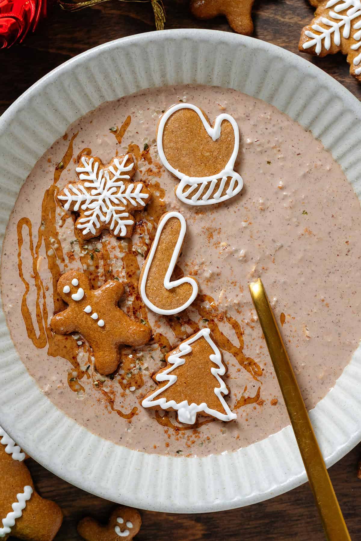 A ceramic beige bowl with creamy thin overnight oats garnished with almond butter and small gingerbread cookies.