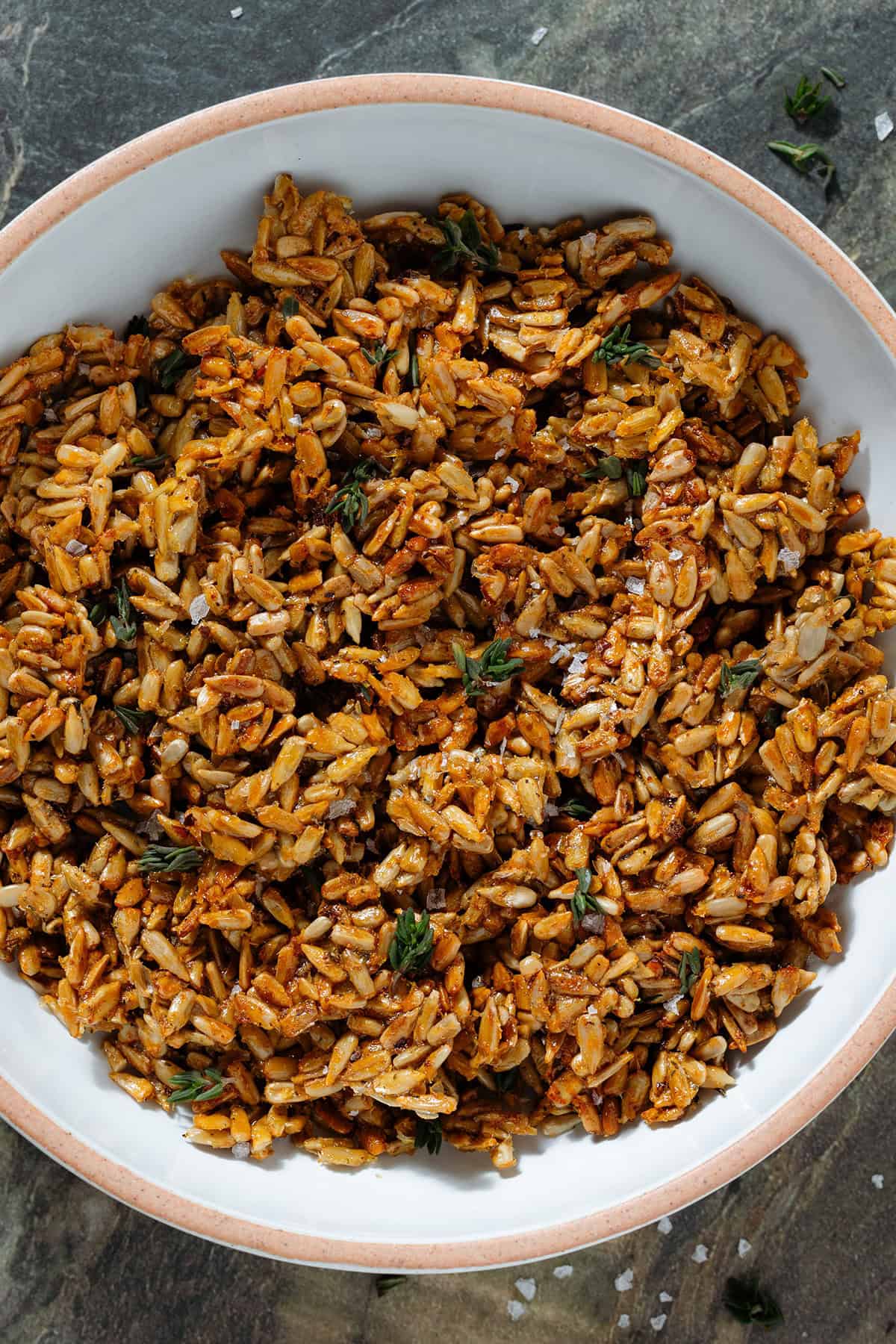 Golden honey roasted sunflower seed clusters garnished with fresh thyme in a white bowl with a beige rim.