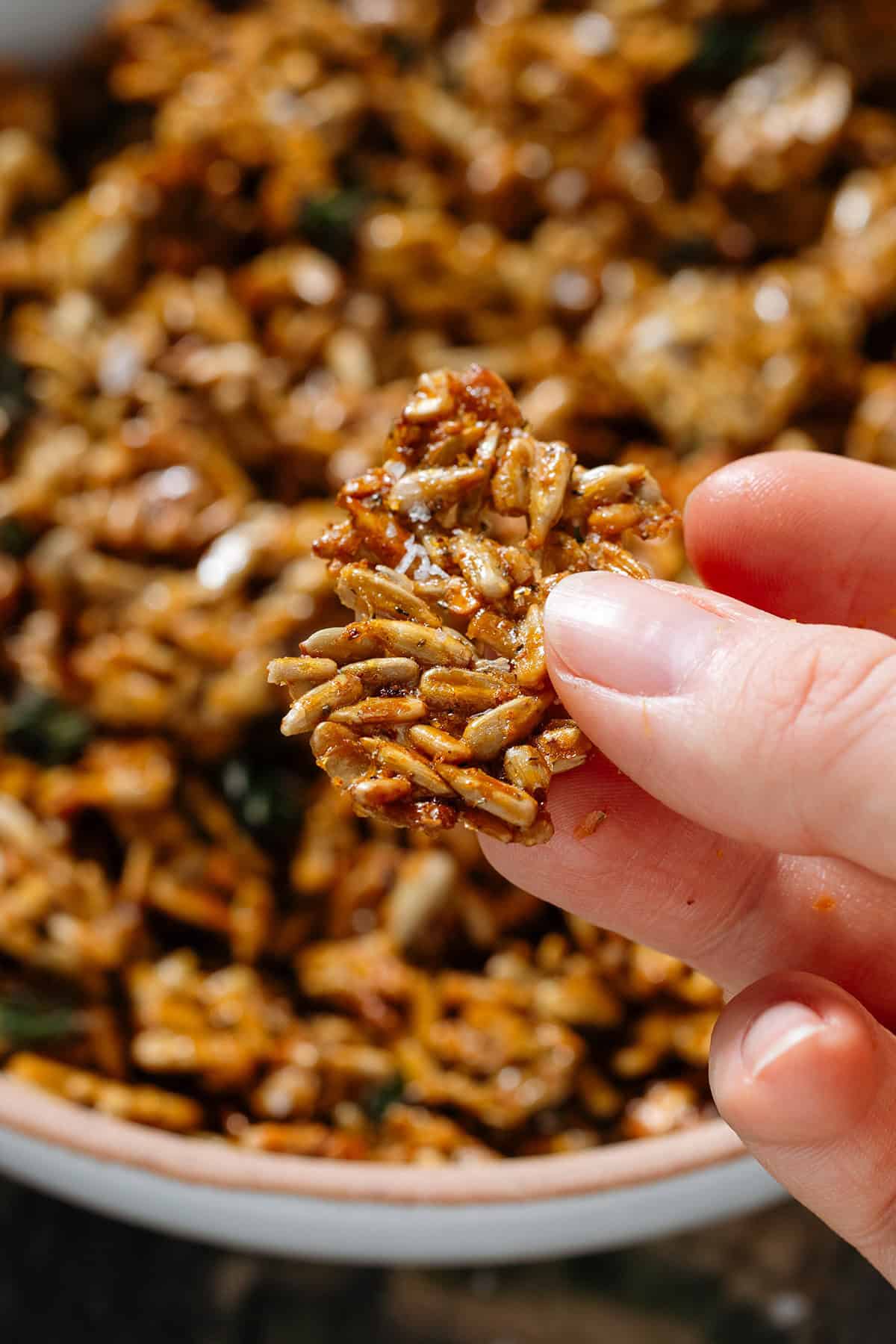 A hand holding a cluster of honey roasted sunflower seeds sprinkled with flaky sea salt.