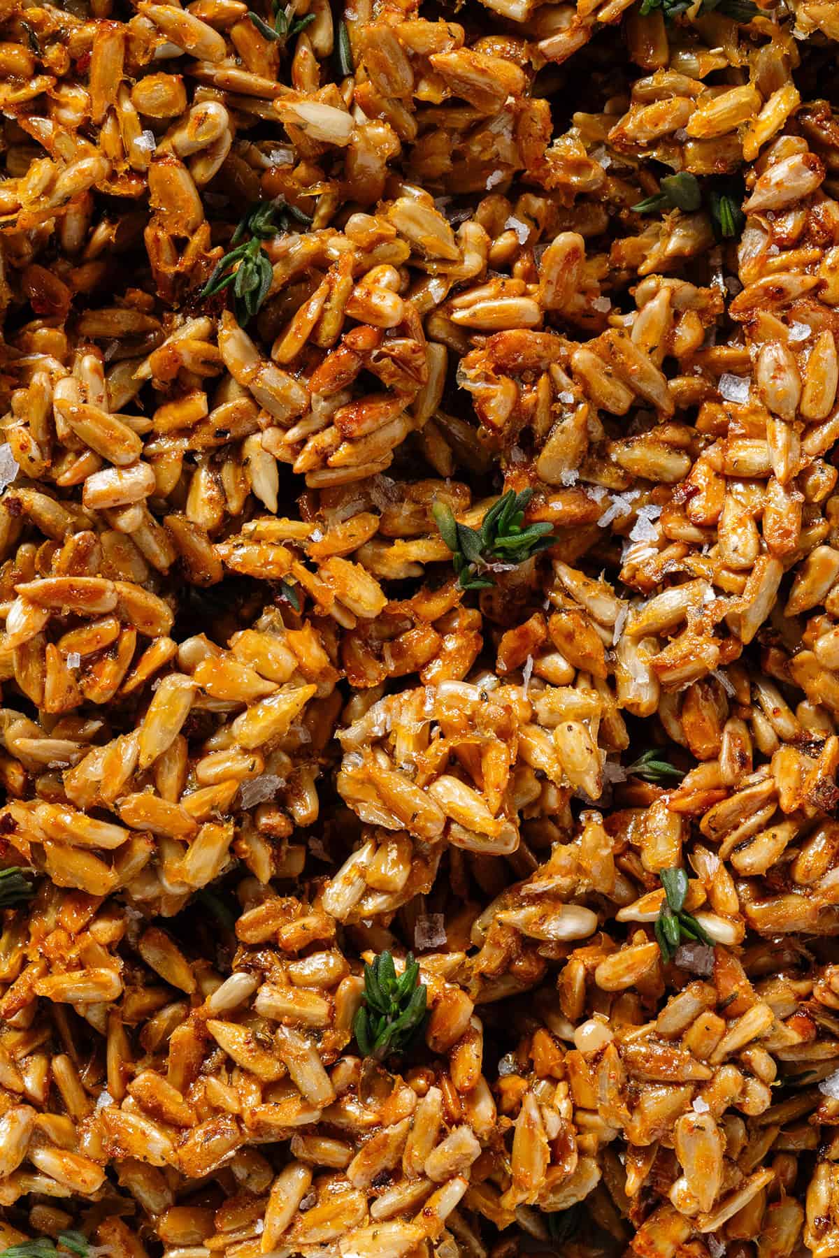 Golden honey roasted sunflower seed clusters garnished with fresh thyme and flaky sea salt.