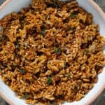 Golden honey roasted sunflower seed clusters garnished with fresh thyme in a white bowl with a beige rim.