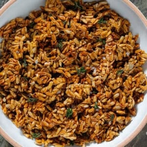 Golden honey roasted sunflower seed clusters garnished with fresh thyme in a white bowl with a beige rim.