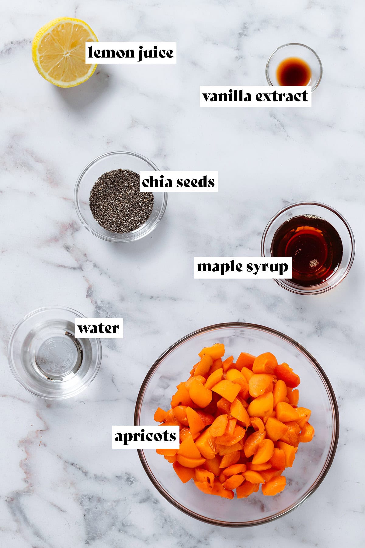 Small glass bowls with diced apricots, maple syrup, chia seeds, water, and vanilla extract, and half a lemon on marble background with text overlay.
