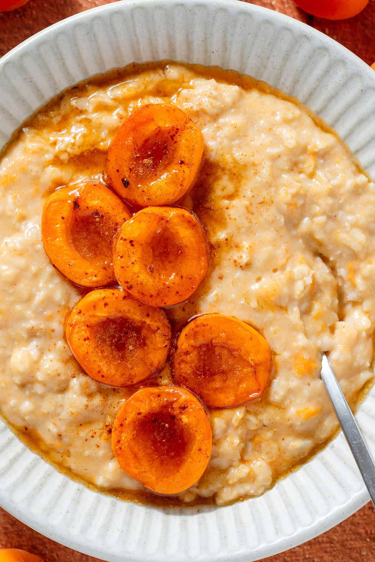 Creamy apricot oatmeal topped with caramelized apricot halves sprinkled with cinnamon in a ceramic bowl with a silver spoon.