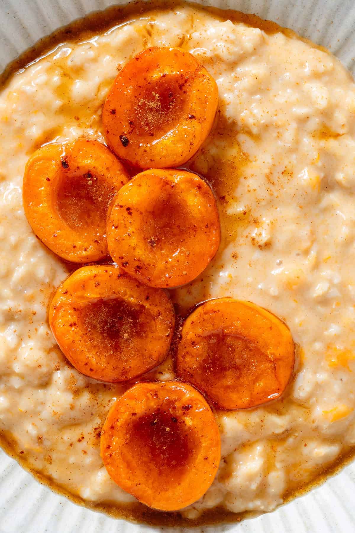 Creamy apricot oatmeal topped with caramelized apricot halves sprinkled with cinnamon and drizzled with the juices from the baked apricots in a ceramic bowl