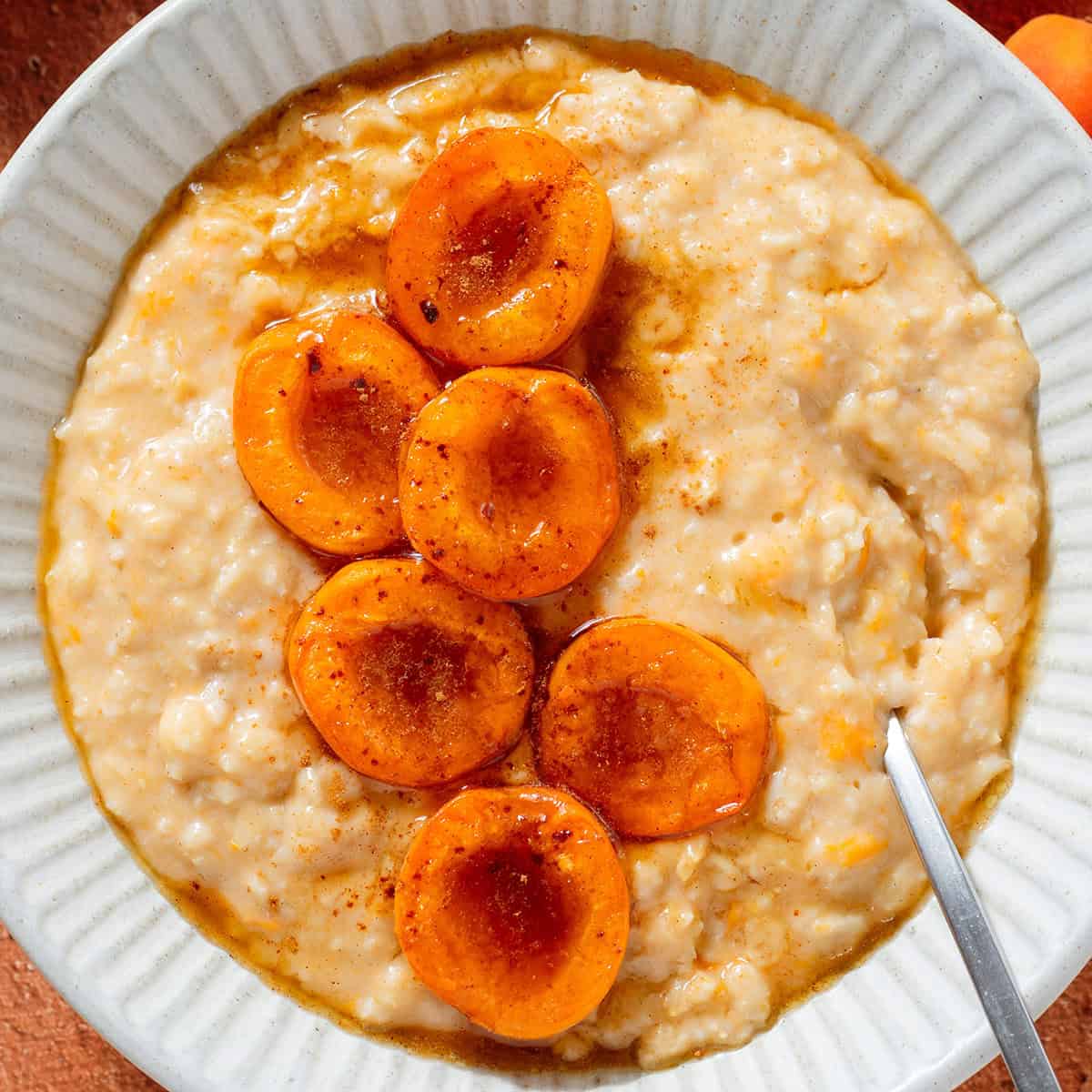 Creamy apricot oatmeal topped with caramelized apricot halves sprinkled with cinnamon in a ceramic bowl with a silver spoon.
