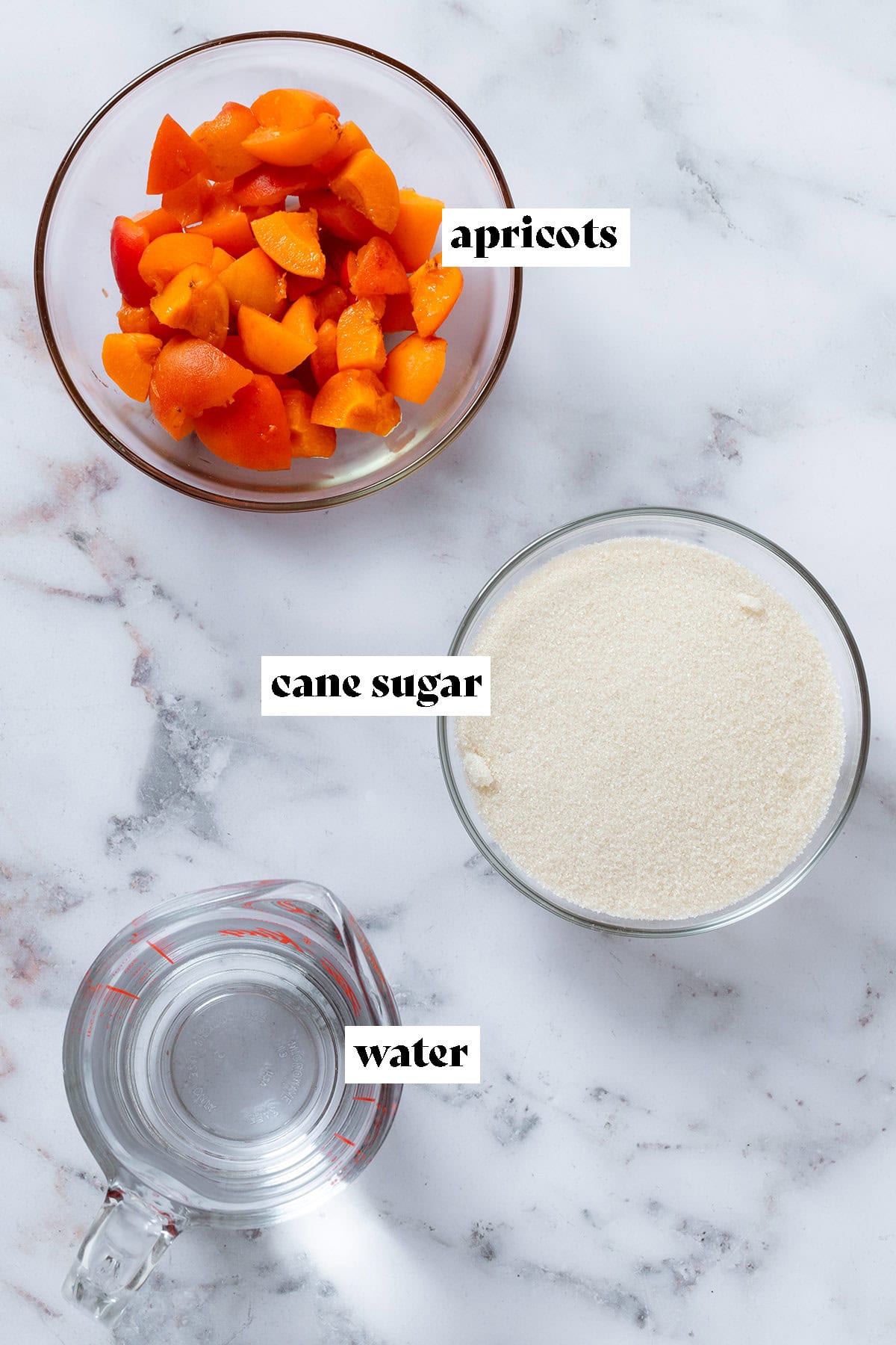 Glass bowls with chopped fresh apricots, cane sugar, and water on a marble background with text overlay.