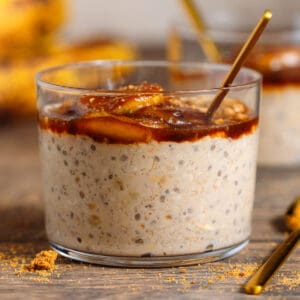 A short glass with brown sugar overnight oats with chia seeds topped with caramelized banana and more sugar with a gold spoon next to the glass.