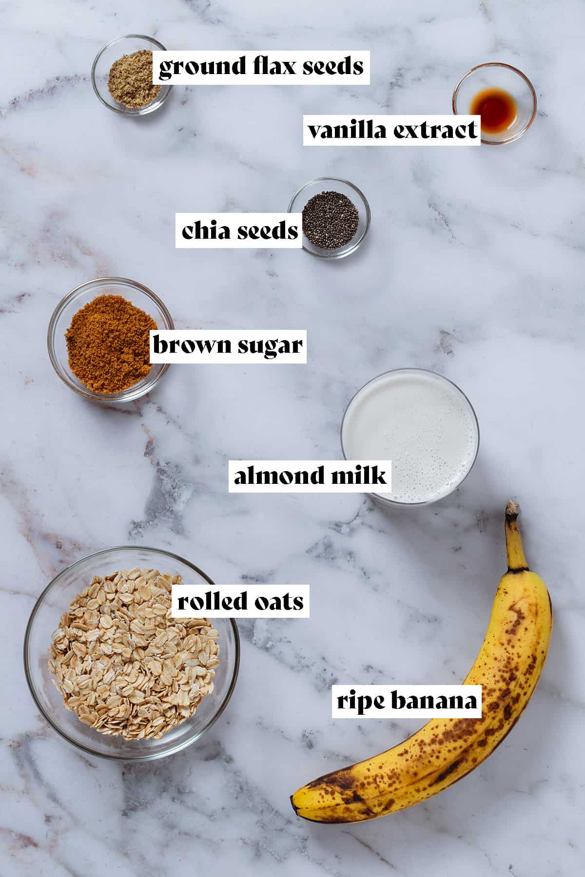 Ingredients like oats, almond milk, brown sugar, and maple syrup in glass bowls and a banana with text overlay.