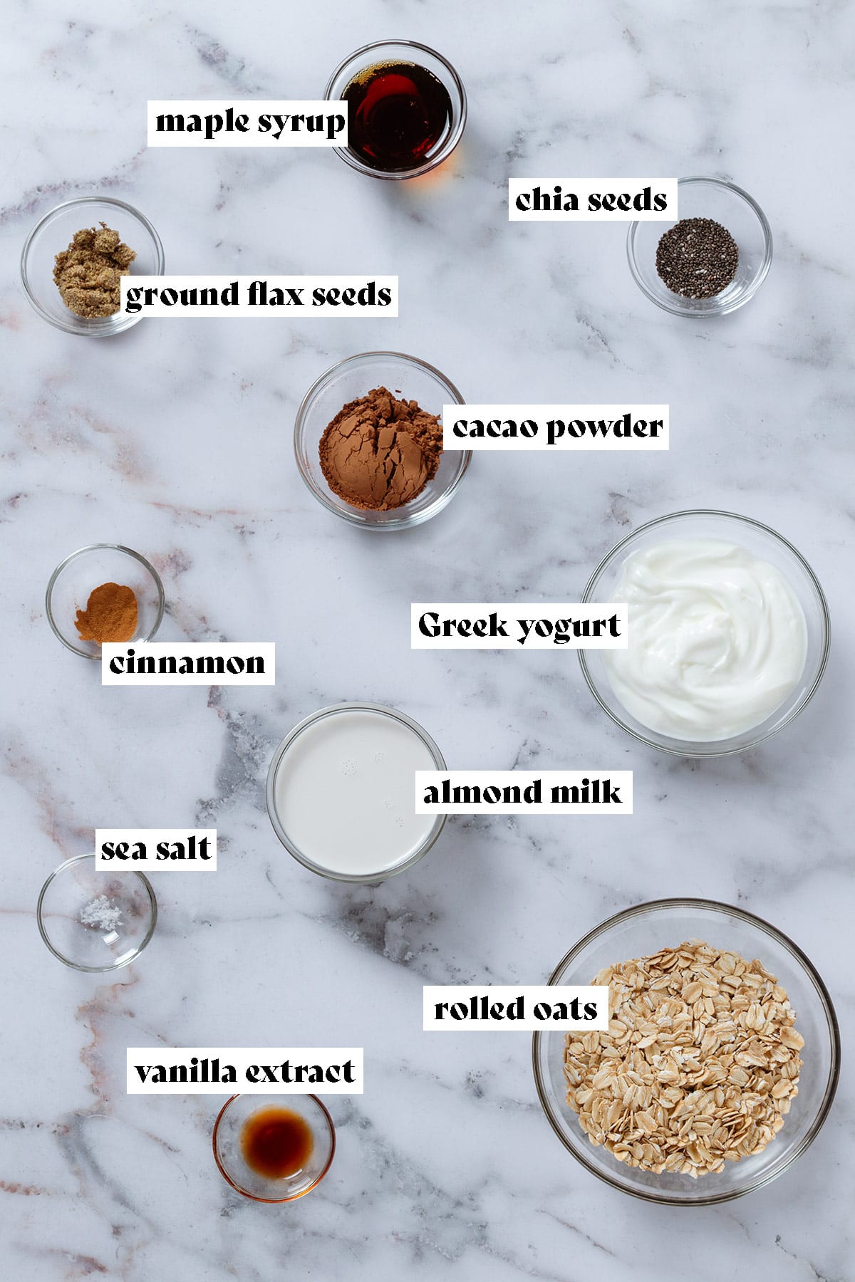 Small glass bowls with ingredients like rolled oats, Greek yogurt, almond milk, cacao powder, and spices with text overlay.