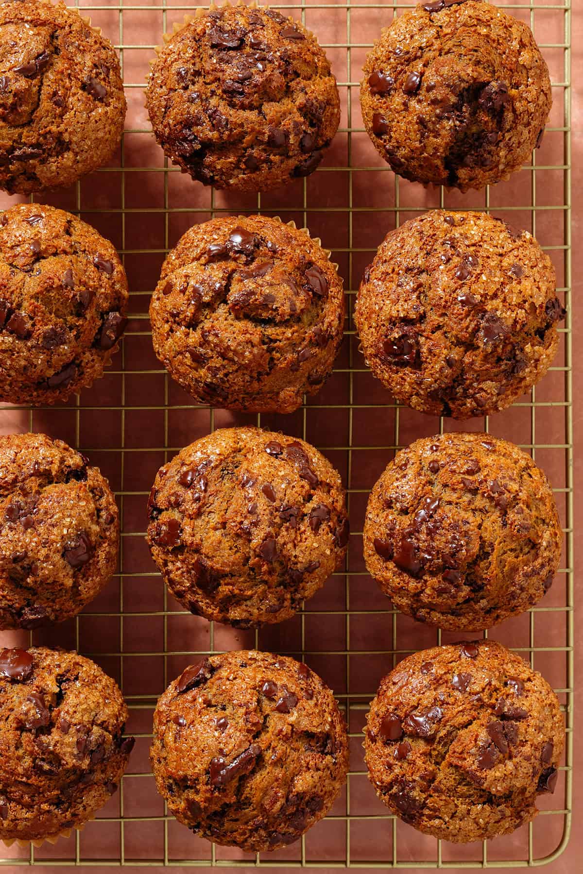Golden chocolate chunk muffins on a golden cooking rack.