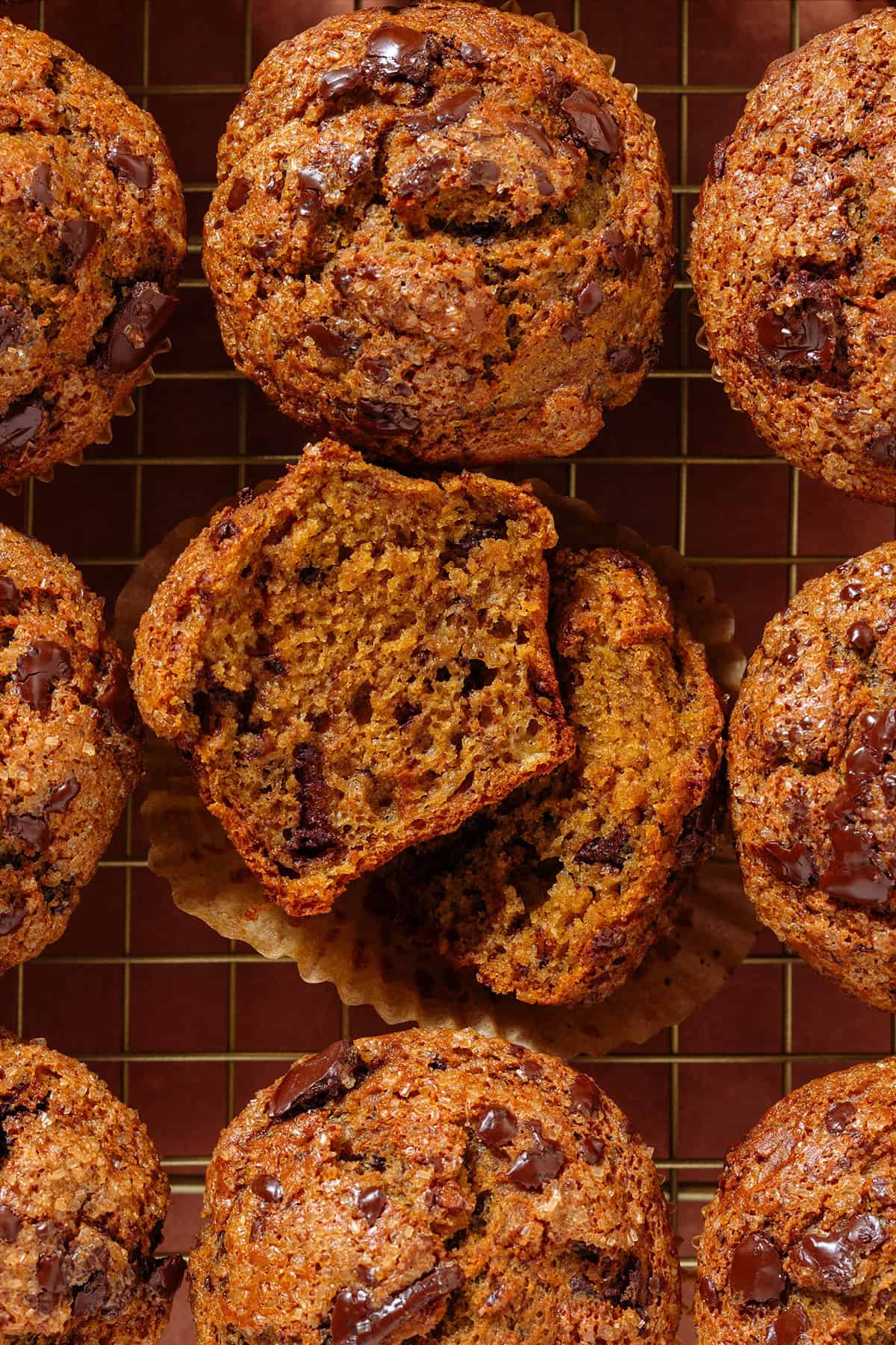 Golden chocolate chip muffins on a cooling rack with the muffin in the middle sliced in half to show the fluffy inside.