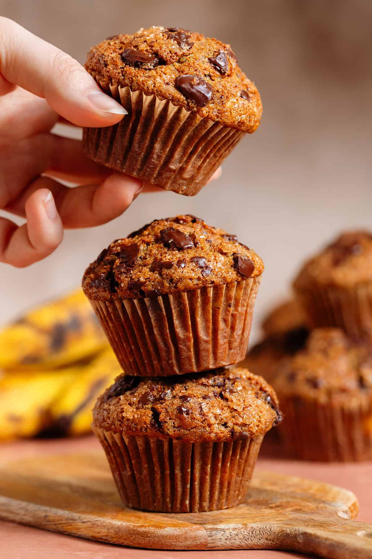 Three chocolate chunk muffins stacked on top of each other and a hand grabbing the top one.