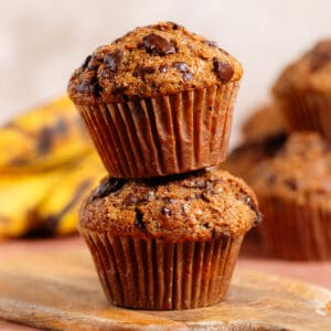 Two chocolate chunk muffins stacked on top of each other on a small wooden cutting board.