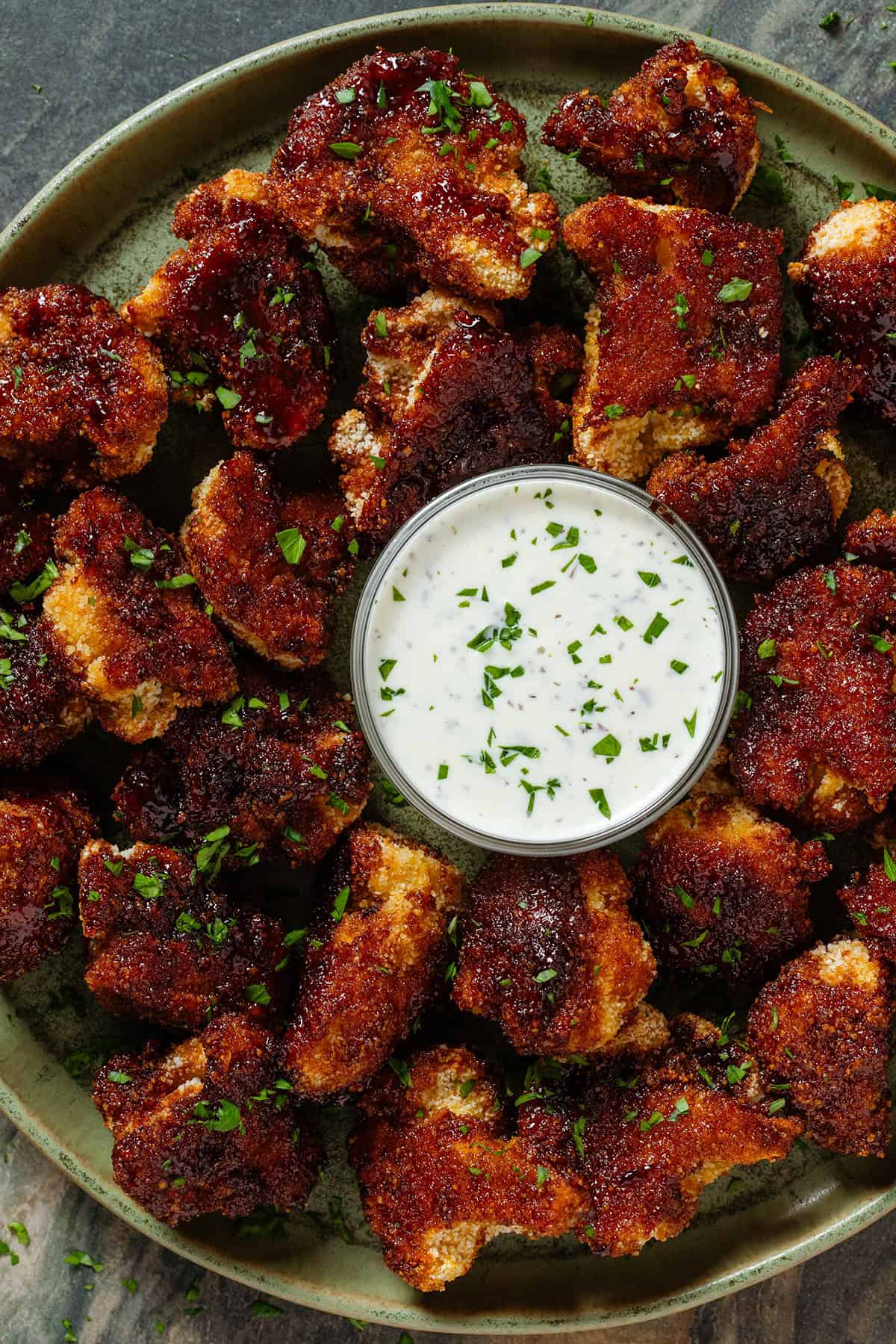 Baked breadcrumbed bbq cauliflower florets on a green plate with a small glass bowl of jalapeno mayo dip in the middle.