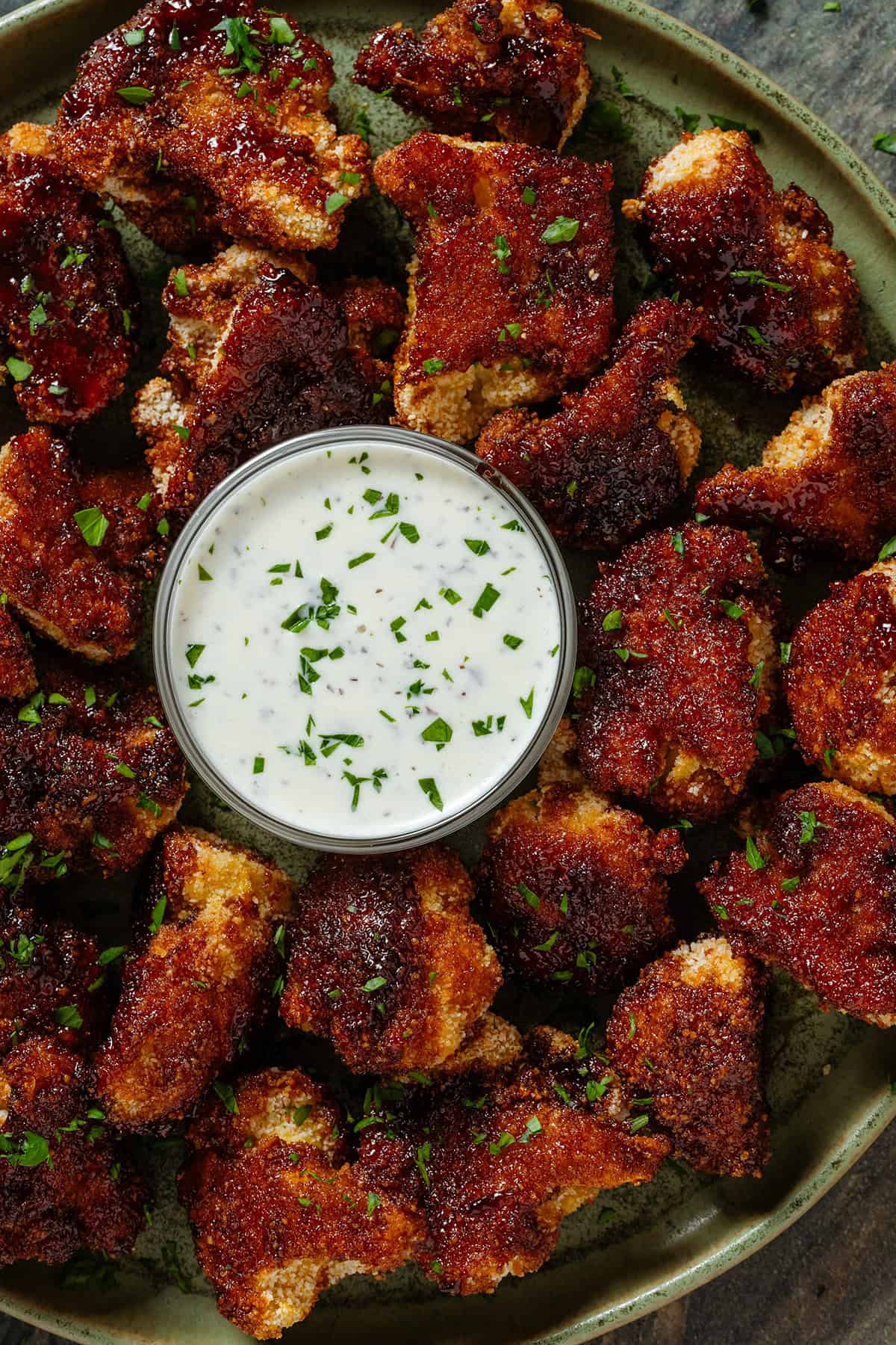 Baked bbq cauliflower wings on a green plate with a small glass bowl of jalapeno mayo dip in the middle.