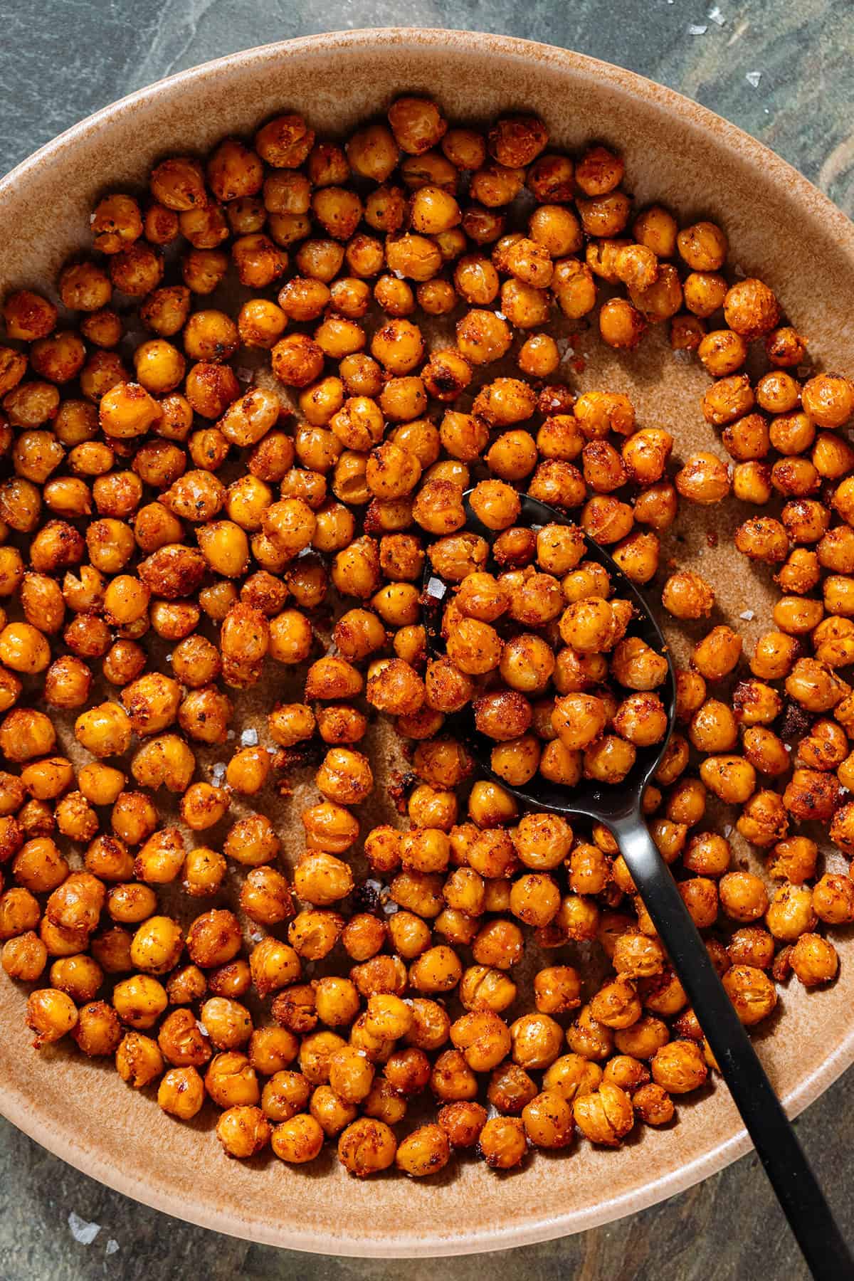 Golden roasted chickpeas with spices in a brown low bowl and a spoon in the bowl.